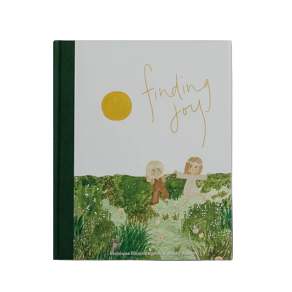 A hardcover book titled 'finding joy' by Monique Ibrahim and Sarah Ried, featuring a light gray cover with a yellow sun, gold script title, and an illustration of two children in a green field.