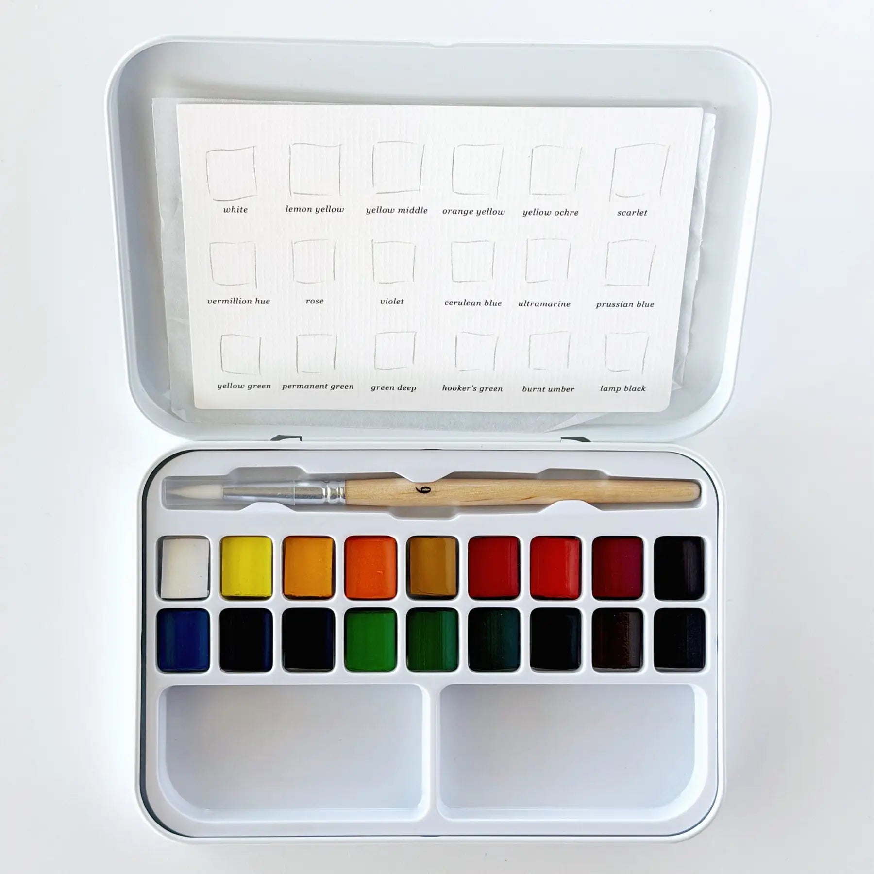 A watercolor paint set in a white metal tin, shown open with 18 color pans, a wooden-handled brush, and a color chart sheet inside the lid on a white background.
