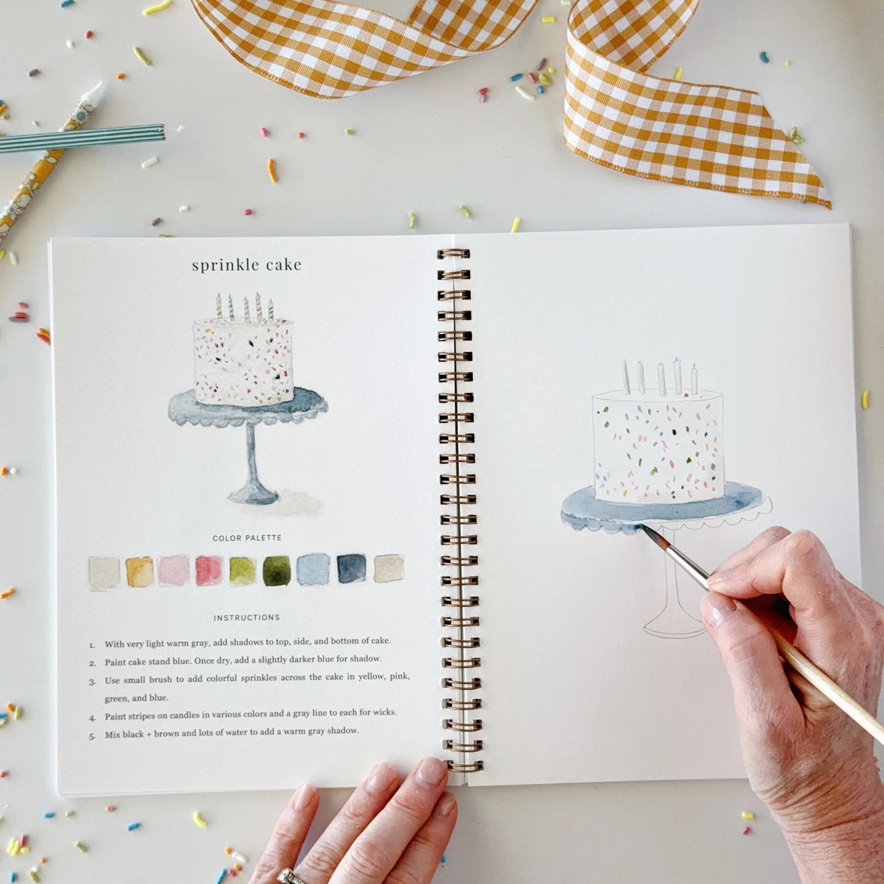 Open book with cake illustration and hand holding a pen