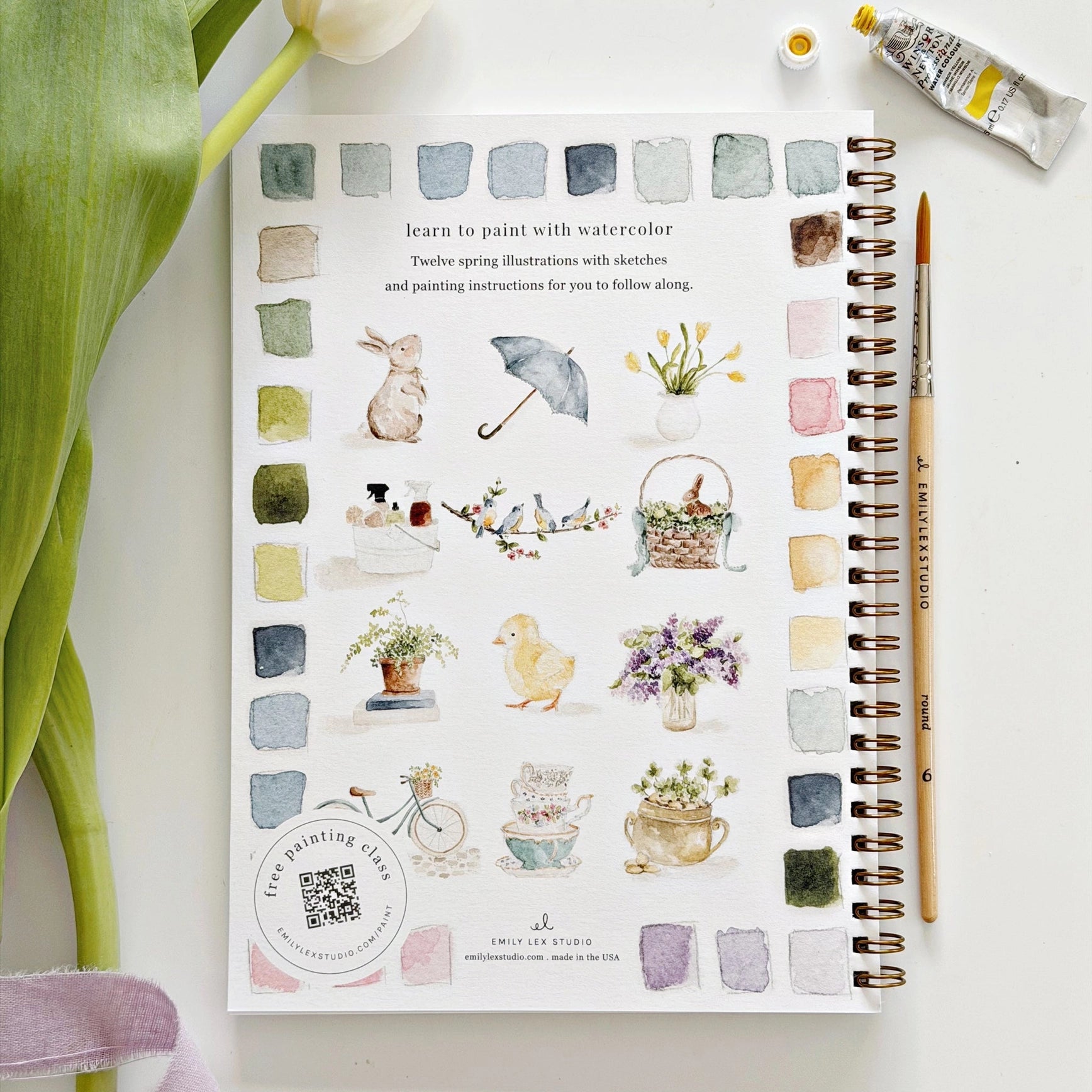 Artistic watercolor illustrations on a book with a paintbrush and watercolor bottle.