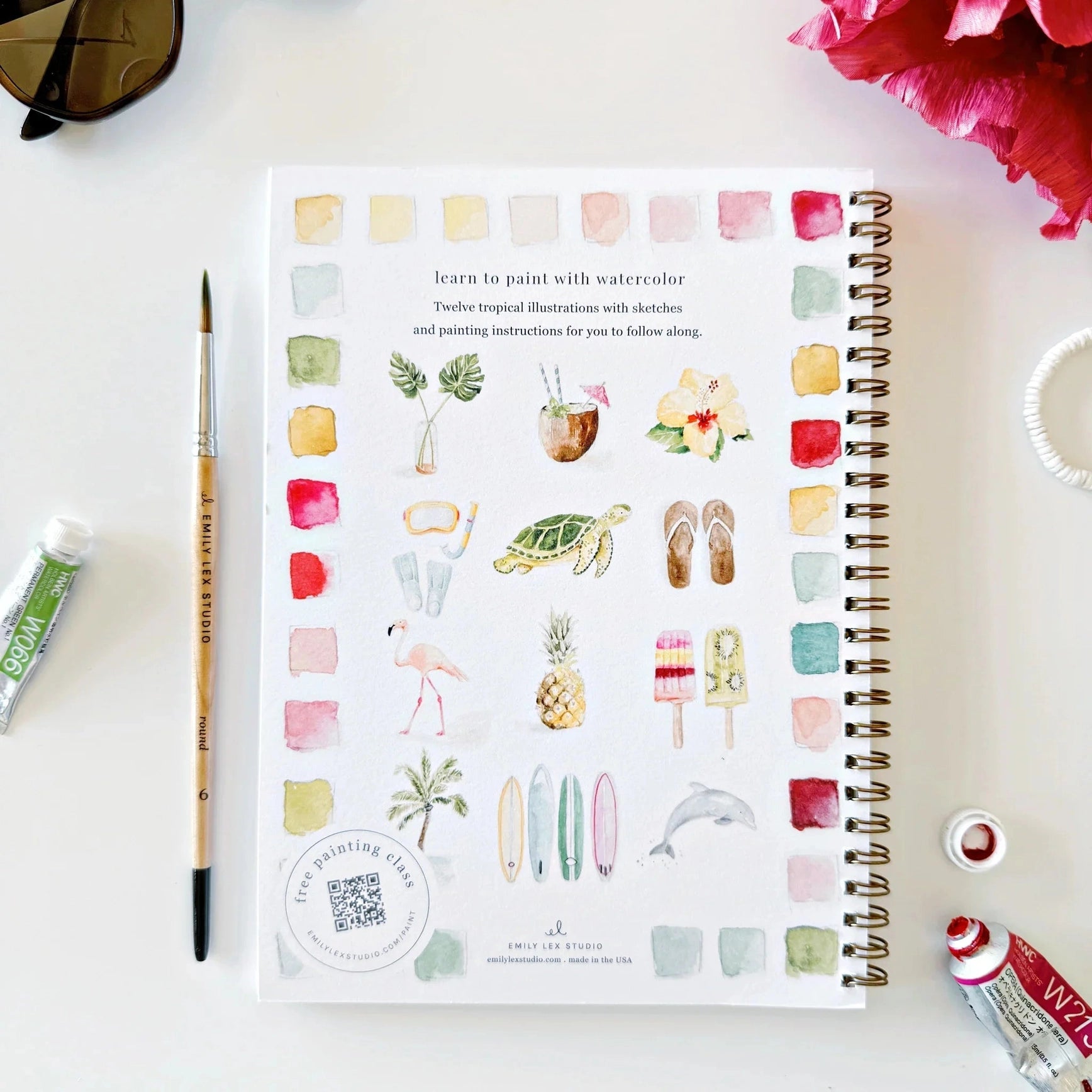 Artistic coloring book with watercolor illustrations on a white surface with art supplies.
