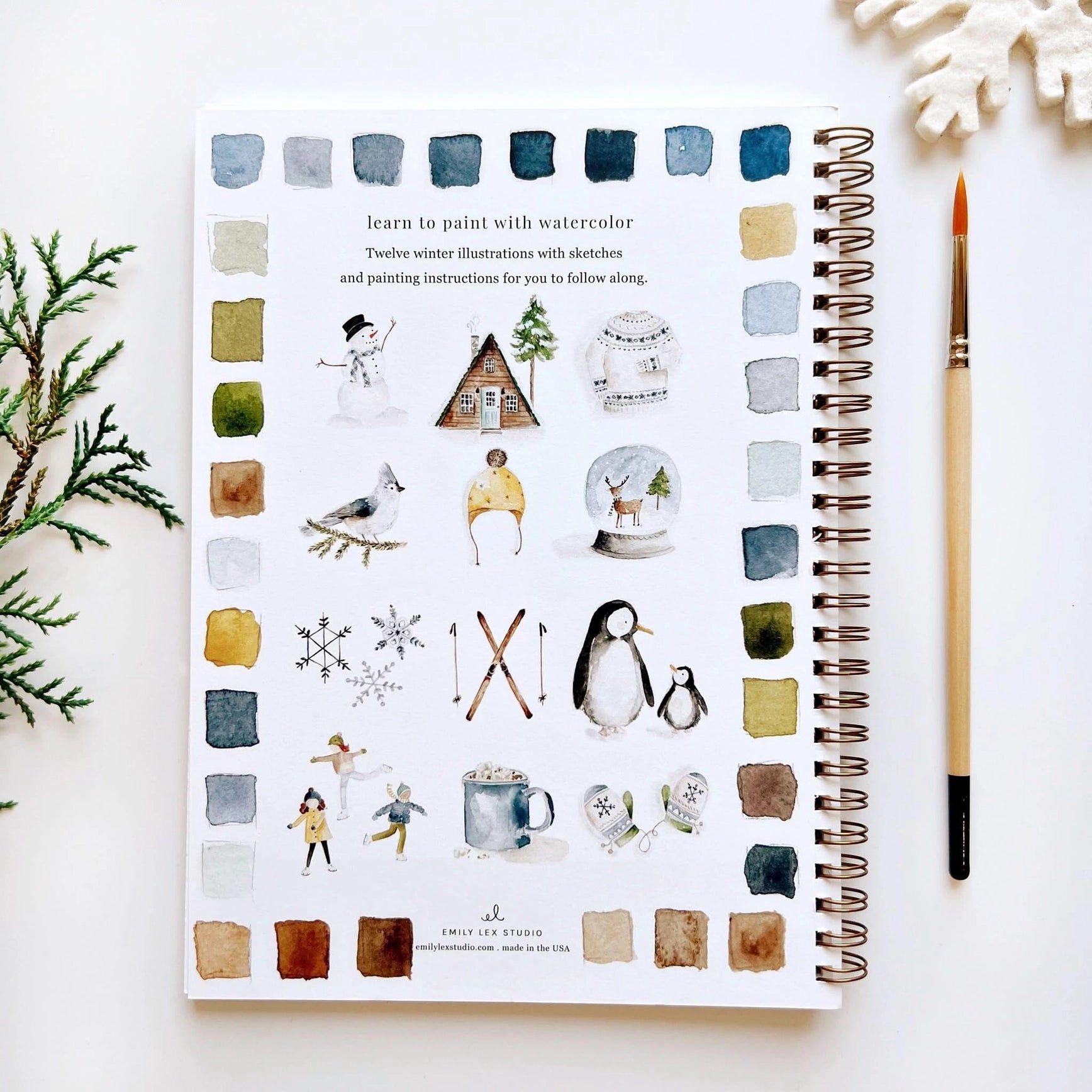 Illustrated notebook with winter-themed illustrations on a white surface with a paintbrush.