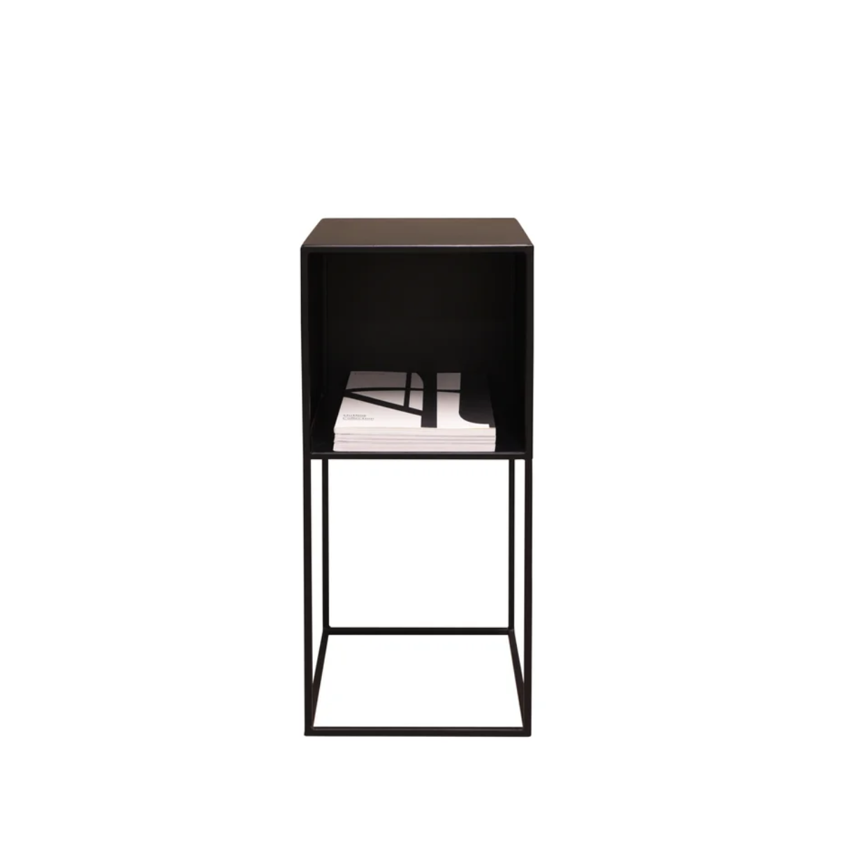 A modern black metal cube side table with an open top shelf holding a stack of magazines, set against a plain white background.