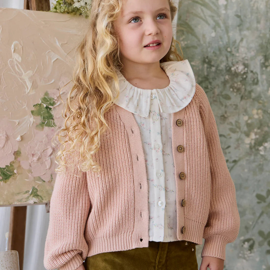 Young girl wearing a pink cardigan over a white blouse with a floral background