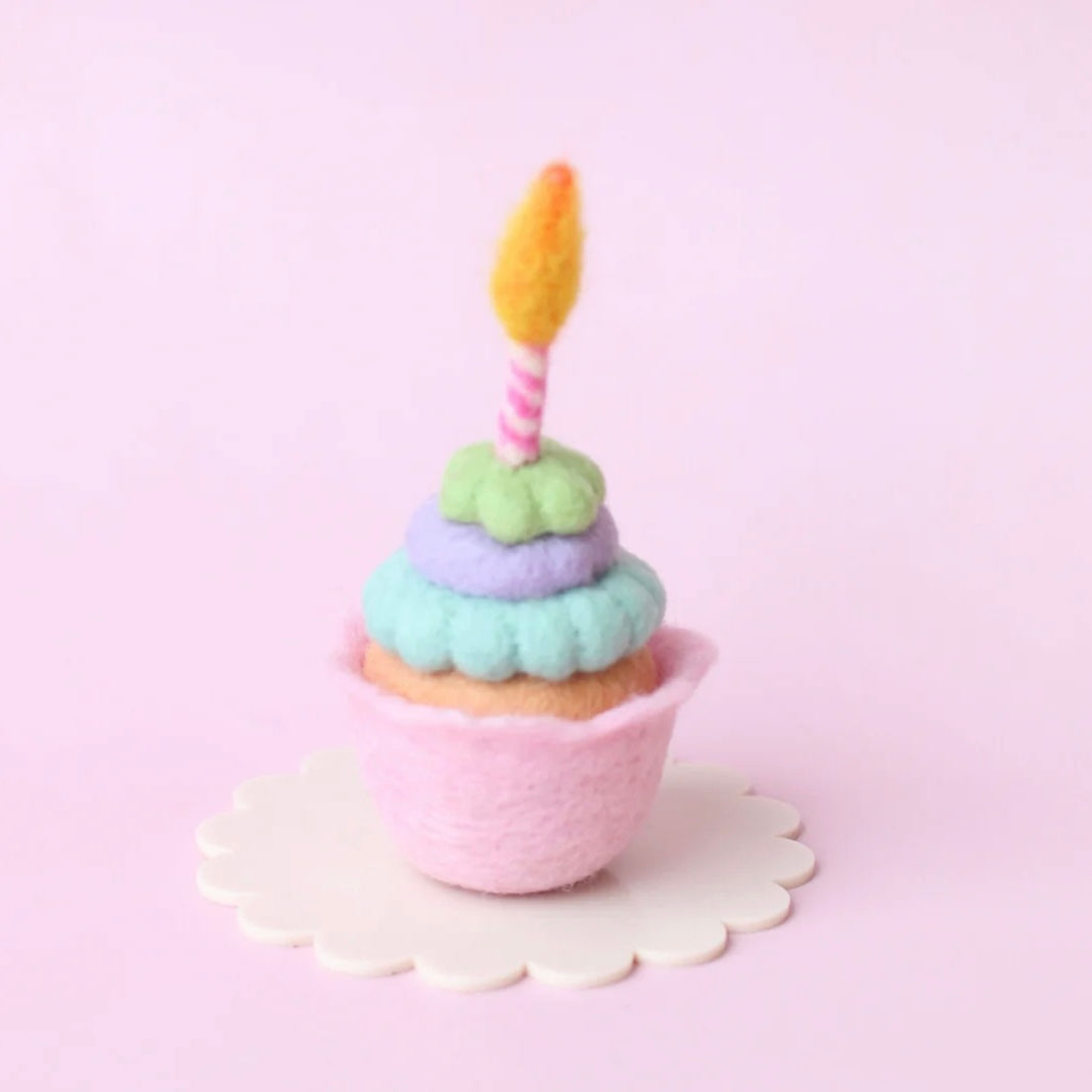 Pastel-colored cupcake with a candle on a pink background