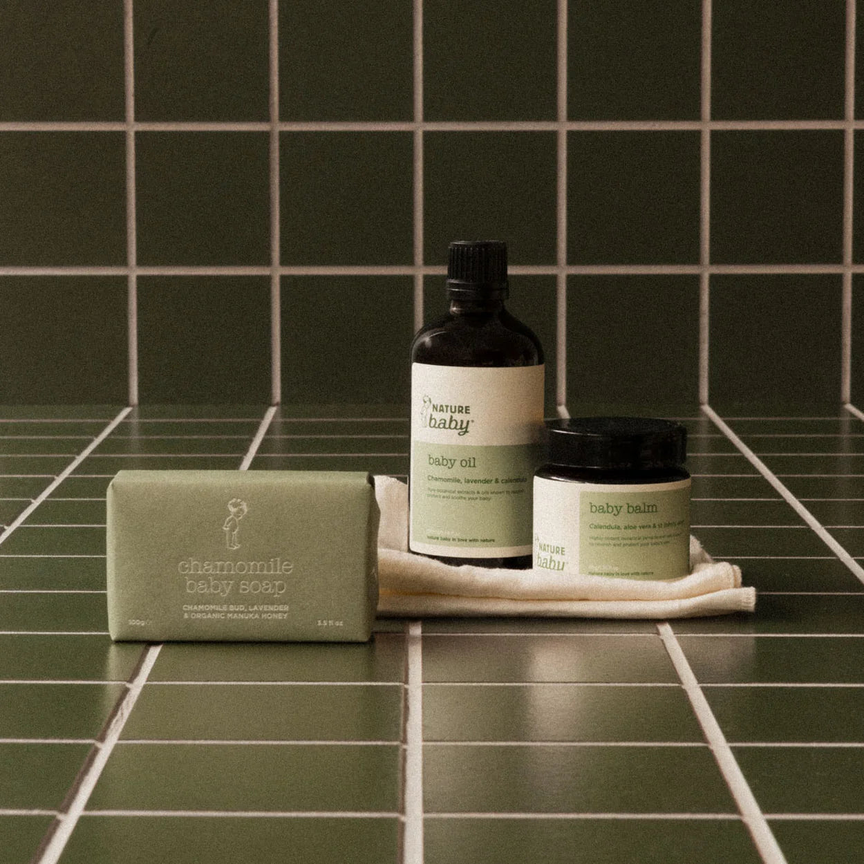 Baby care products including oil, balm, and soap on a tiled bathroom counter.