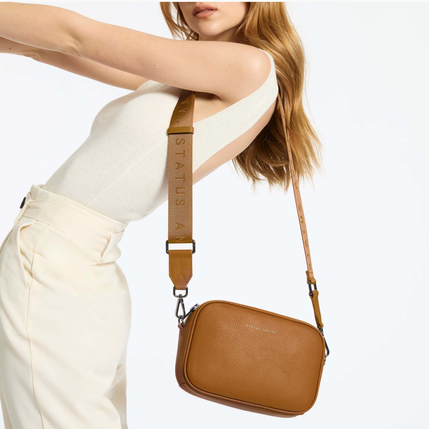 Woman wearing a brown leather bag with 'STATUS' branding on a white background