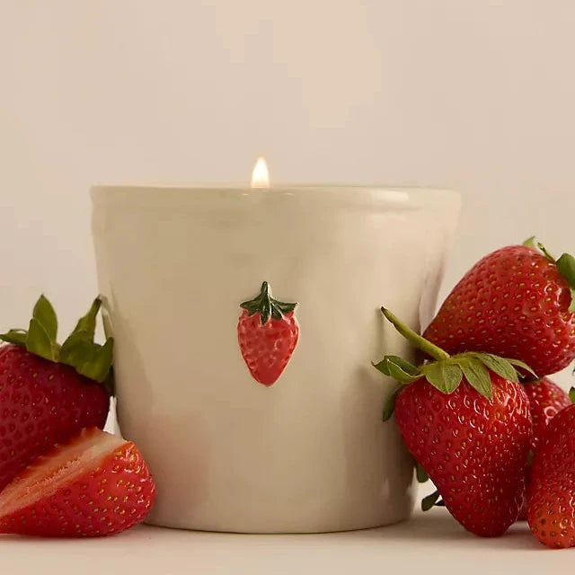 Candle with strawberry design surrounded by real strawberries on a neutral background