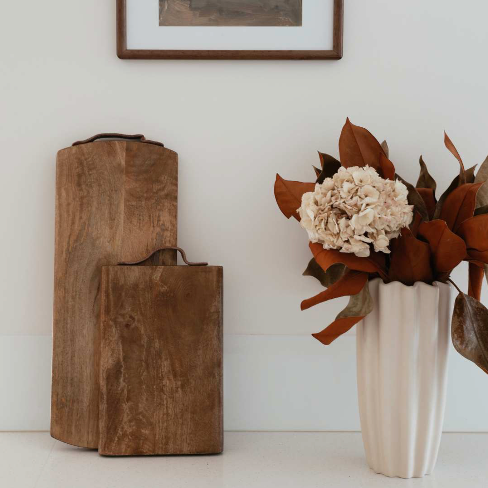 Wooden serving board and vase with flowers on a white surface