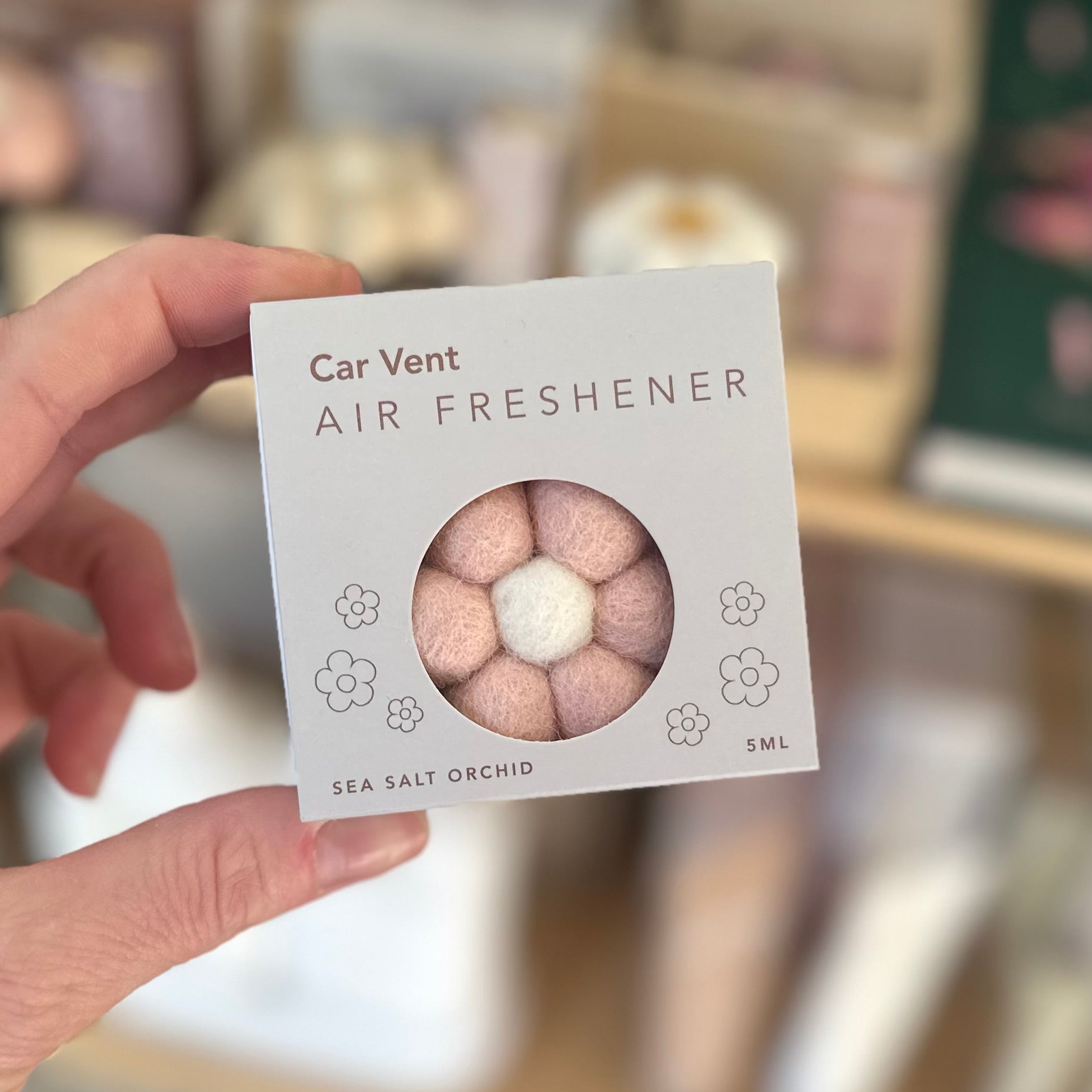 Hand holding a car vent air freshener packaging with a blurred background