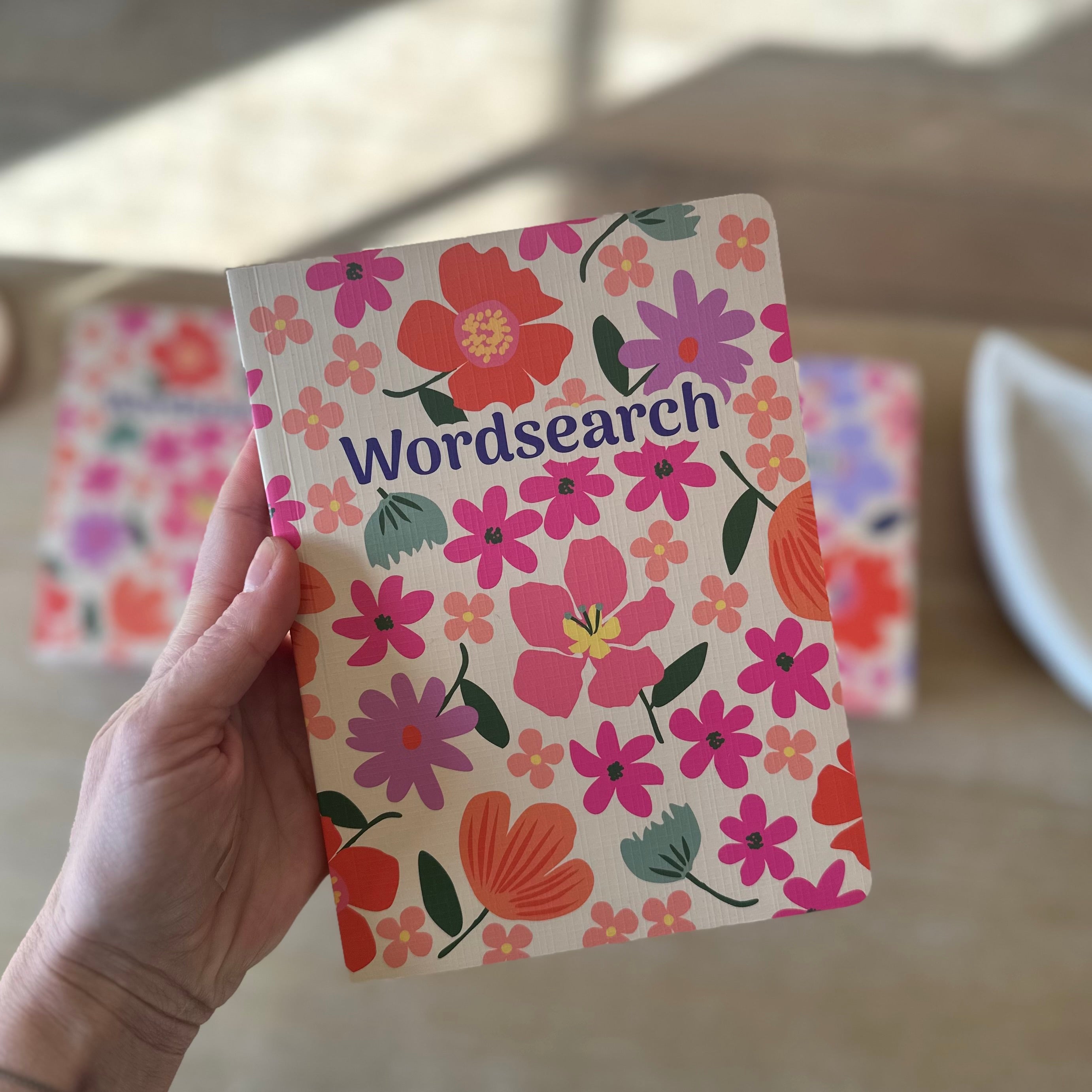 Hand holding a 'Wordsearch' book with floral cover design.