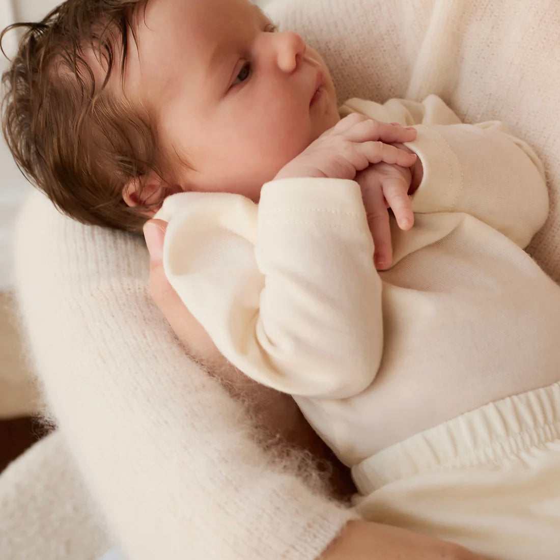 Baby in a cream-colored outfit lying on a soft surface