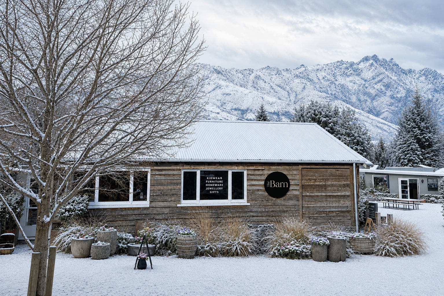 Wooden building with 'The Barn' sign in a snowy landscape with The Remarkables mountains range