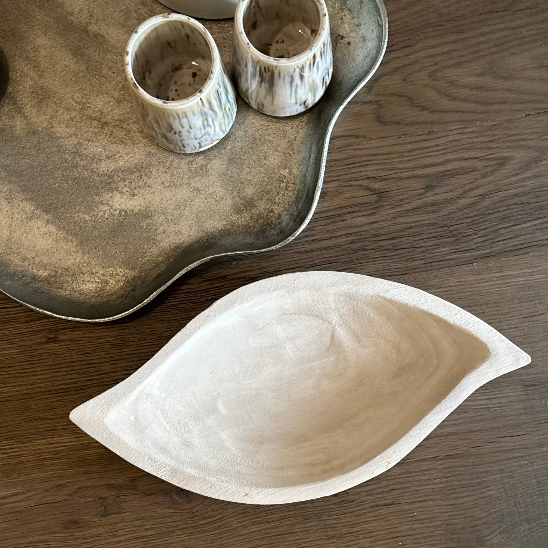Ceramic leaf-shaped dish on a wooden surface with a tray and small cups in the background.