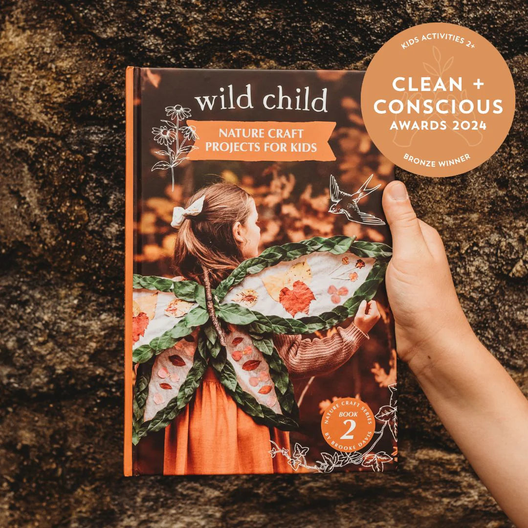 Book titled 'Wild Child' held by a hand on a stone surface, with 'Clean + Conscious Awards 2024' badge.