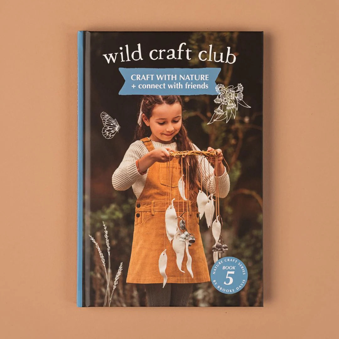 Book titled 'wild craft club' with a girl in an orange dress holding a nature-themed object on a brown background