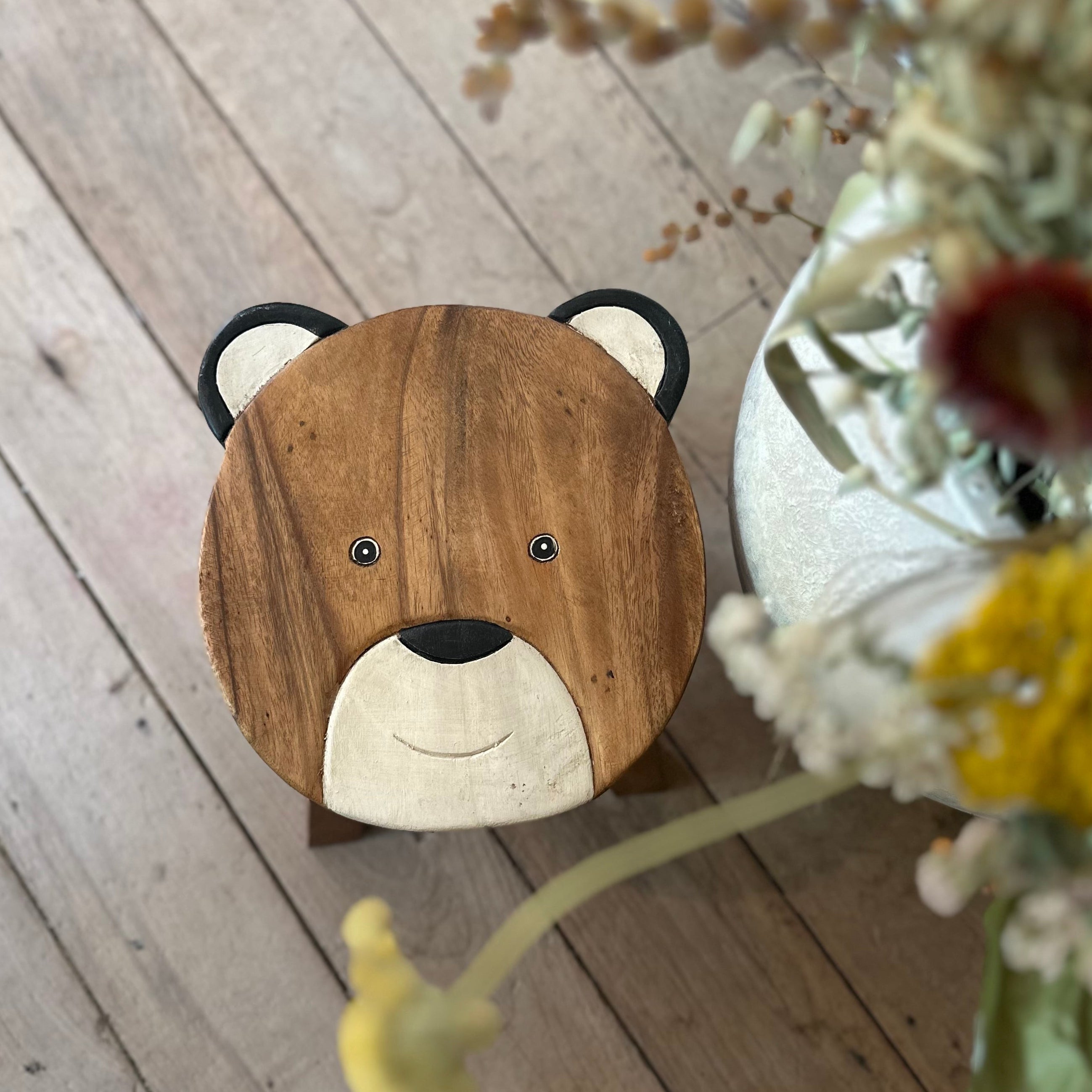 Wooden stool with bear face design on a wooden floor with flowers.