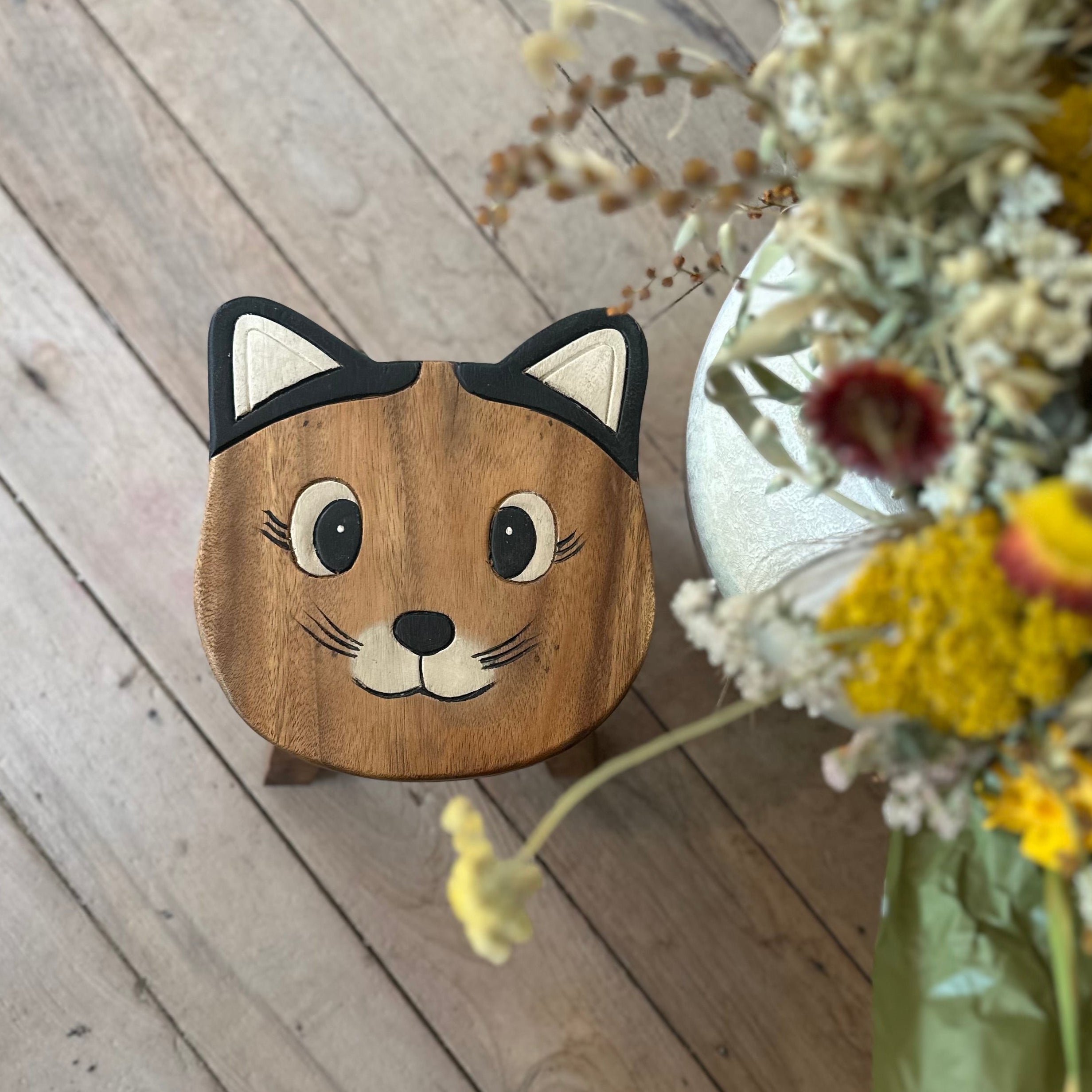 Wooden cat-shaped object on a wooden floor with a bouquet of flowers in the foreground.