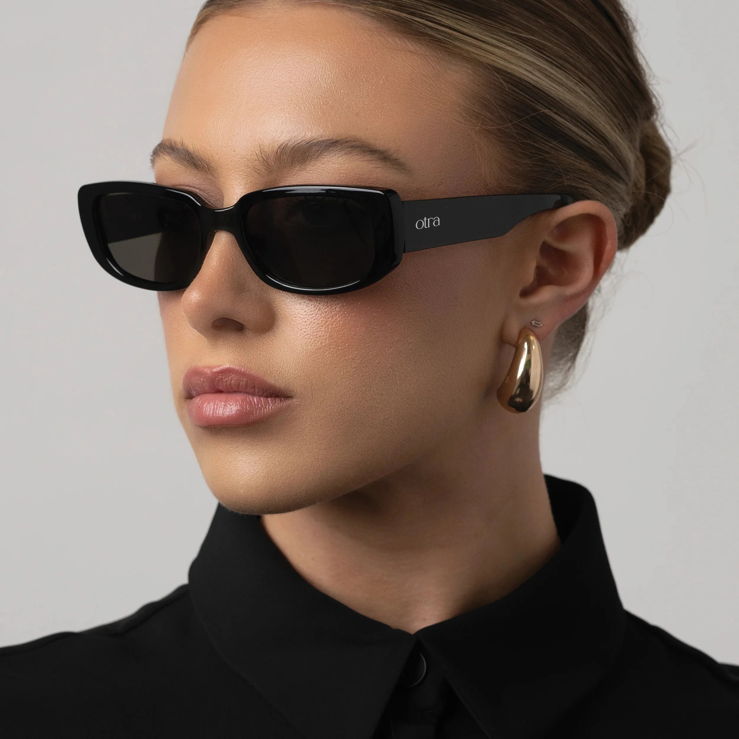 Person wearing black sunglasses and a black outfit against a gray background