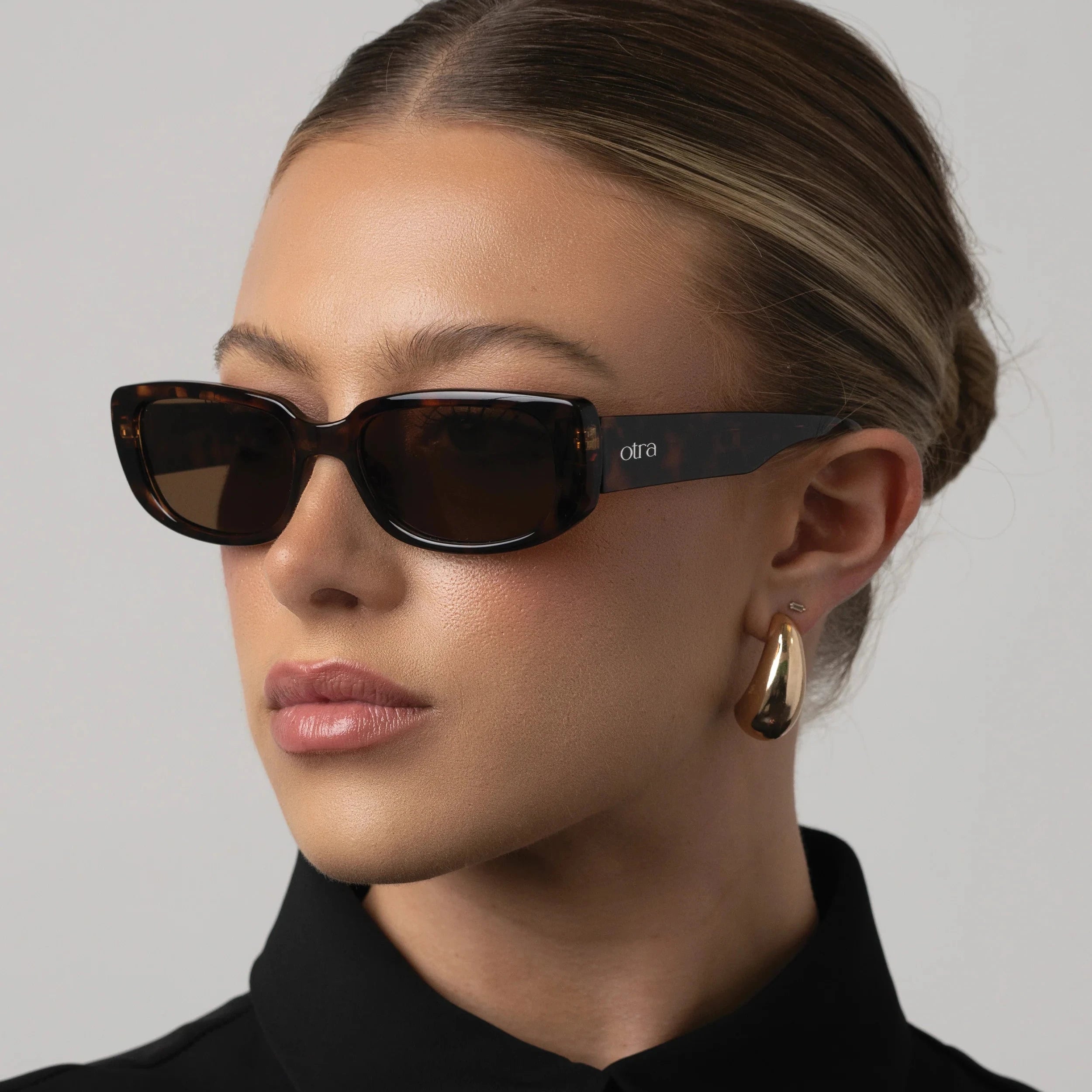 Woman wearing sunglasses and a black outfit against a gray background
