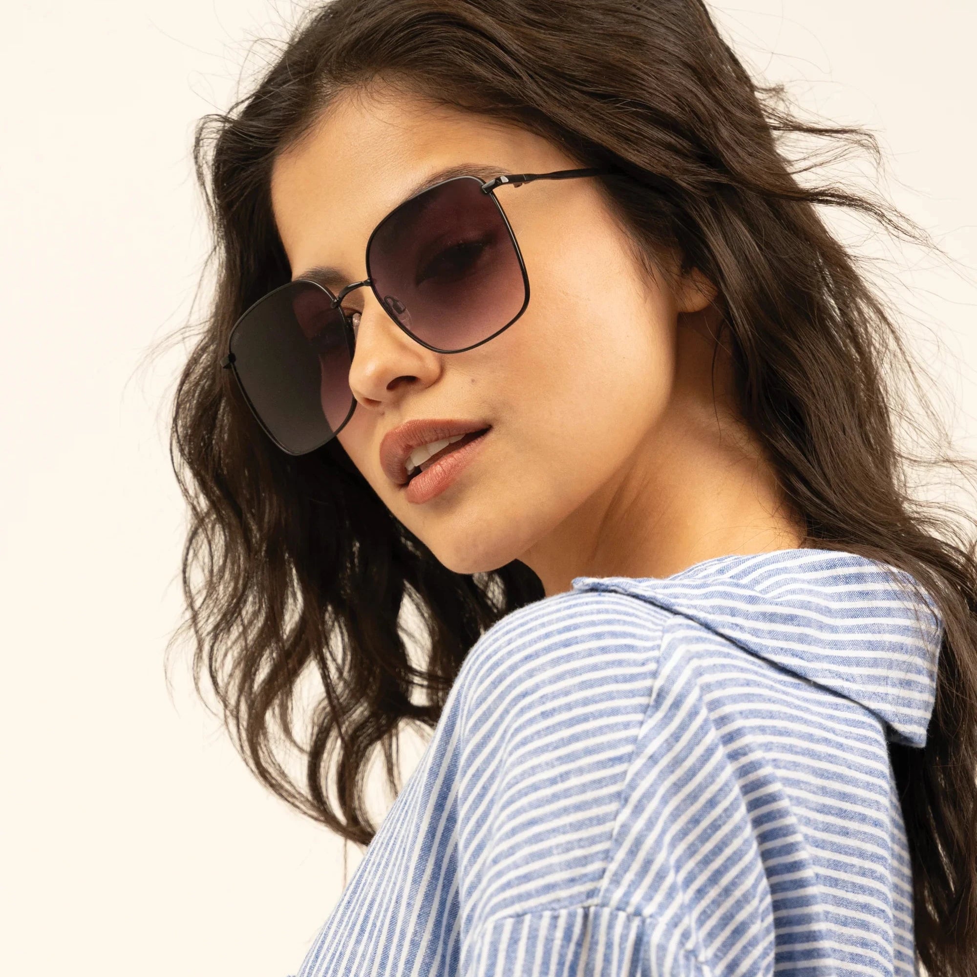 Woman wearing sunglasses and a blue striped shirt against a plain background