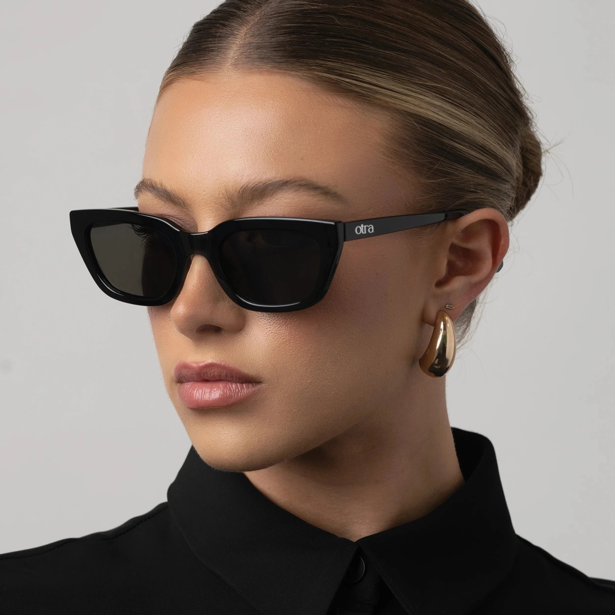 Woman wearing black sunglasses and a black outfit against a gray background