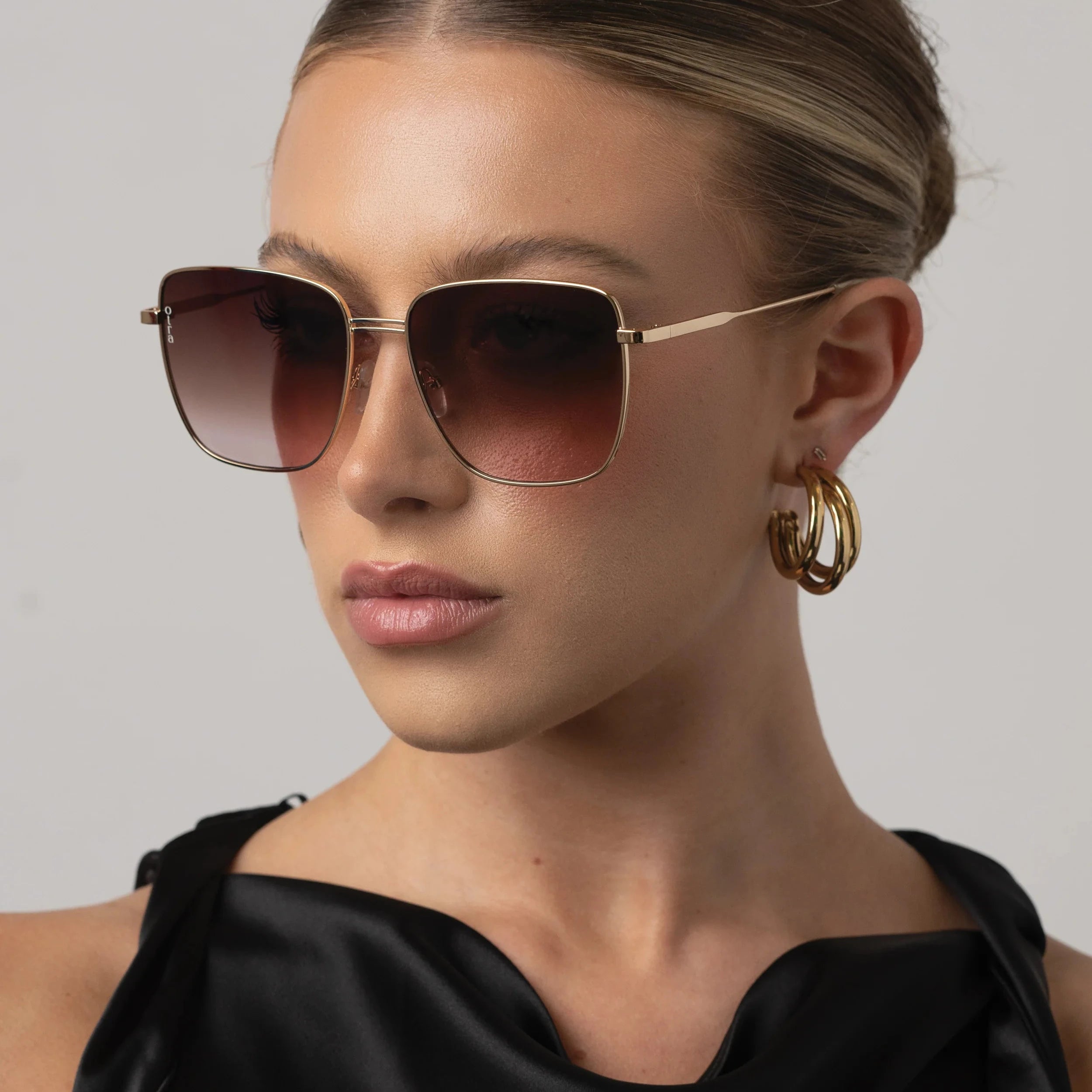 Woman wearing sunglasses and a black top against a neutral background
