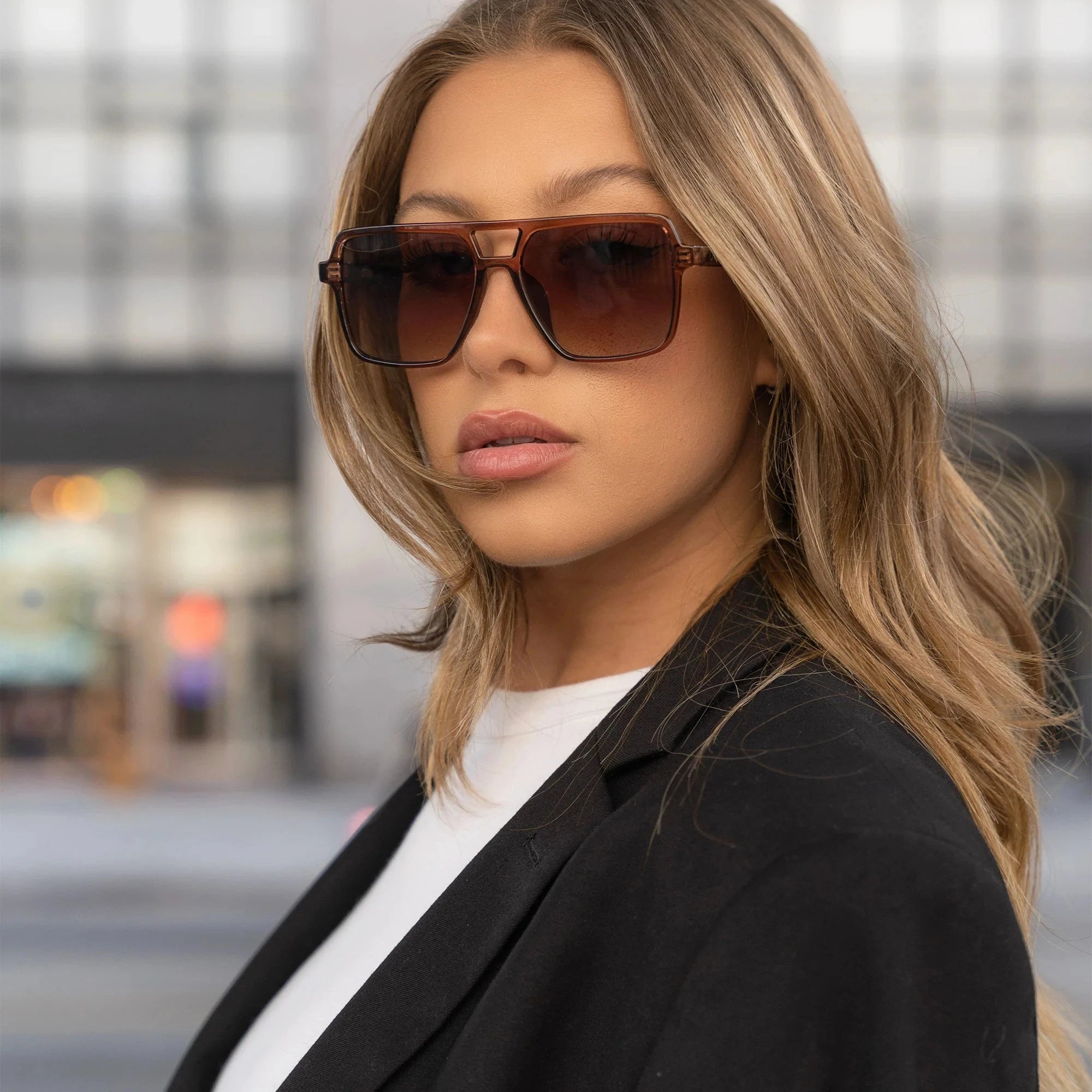Woman wearing sunglasses and a black blazer in an urban setting